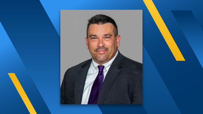 A professional headshot of James J. Branam wearing a dark suit and purple tie. The headshot is floating over a blue and gold diagonal striped background.